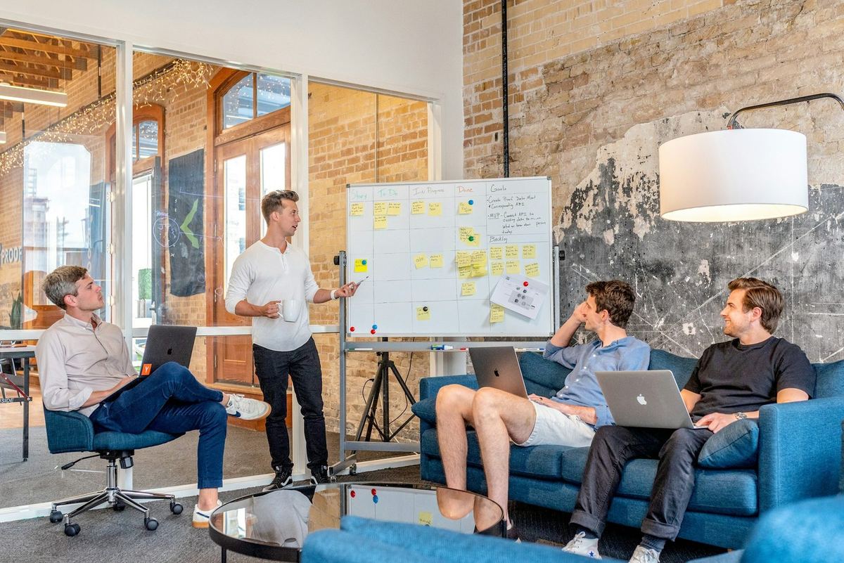 A team lead walking colleagues through a project board in a bright brick office